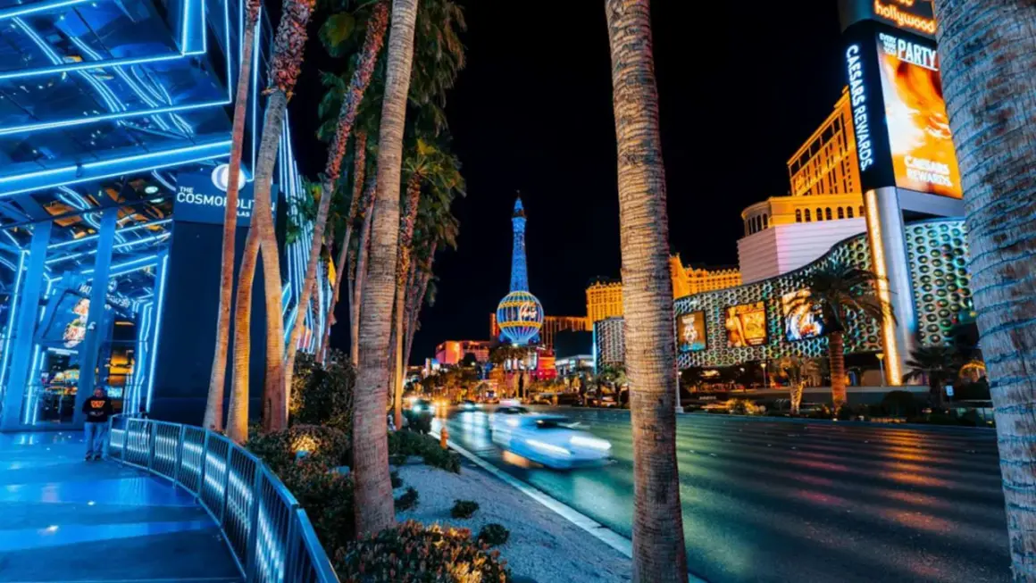 Nocne Las Vegas atrakcje: palmy, neonowe światła, wieża Eiffla i ruch uliczny.
