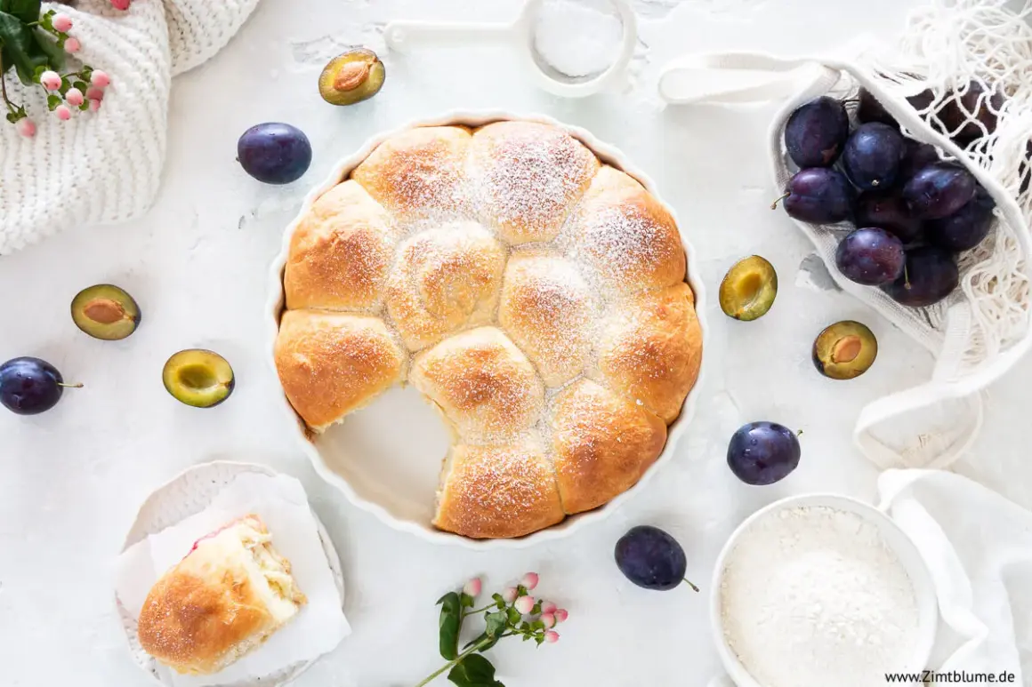 Ein goldbrauner Hefekuchen mit Puderzucker, umgeben von frischen Pflaumen. Perfekt für ein Buchty Rezept!