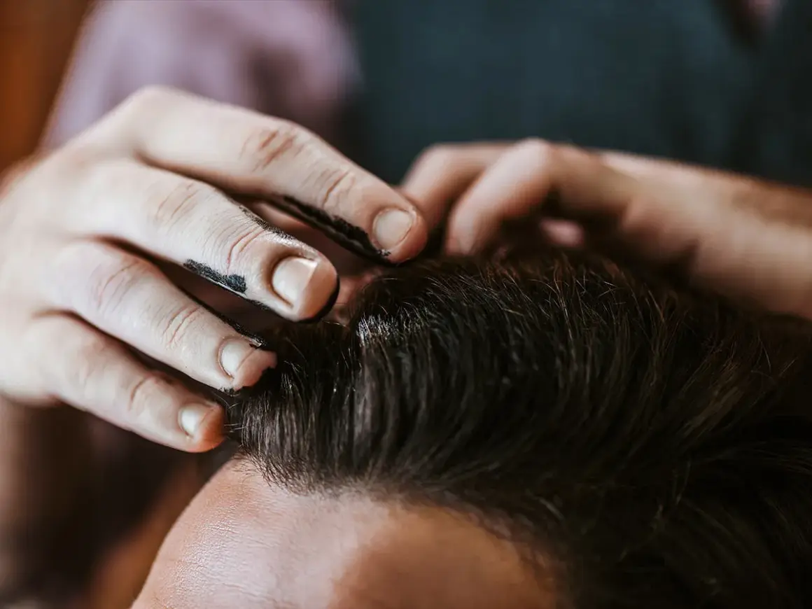 Main d'un coiffeur appliquant du gel ou de la cire sur les cheveux d'un client pour un coiffage parfait.