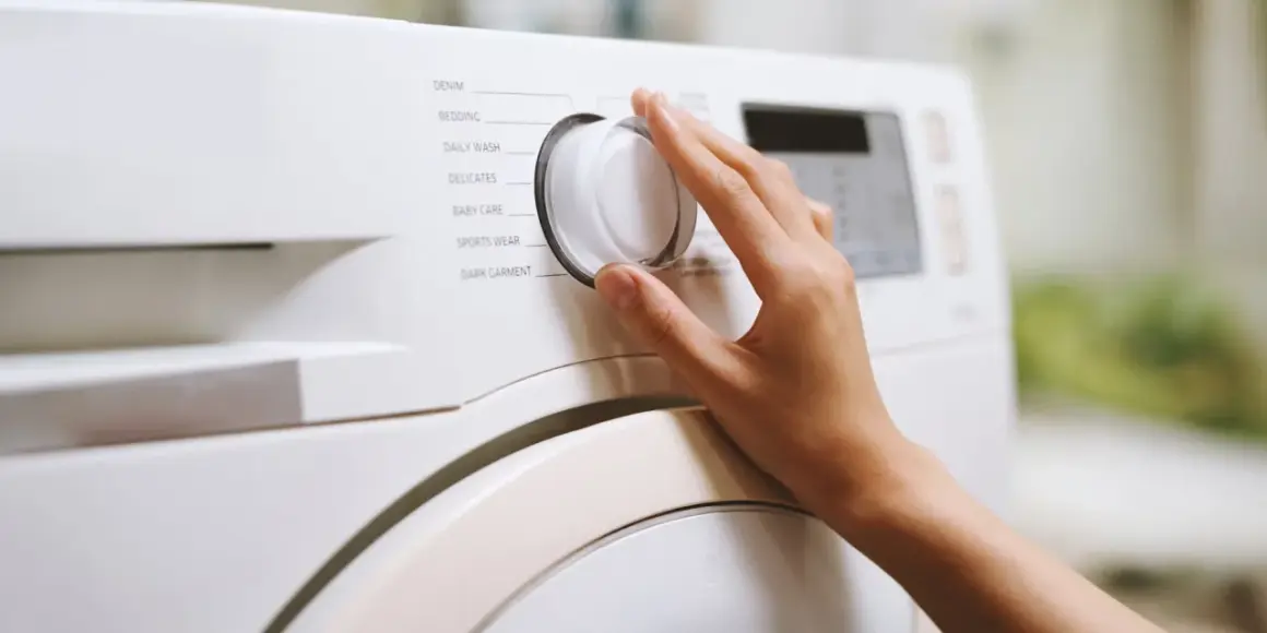 Dłoń kręci pokrętłem pralki, wybierając program "Bedding". Zastanawiasz się, w jakiej temperaturze prać pościel z kory? Sprawdź instrukcję pralki.