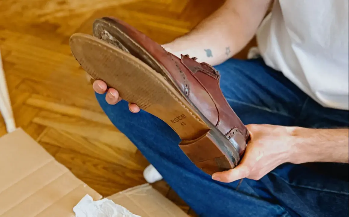 Une personne examine une chaussure en cuir marron, montrant l'usure de la semelle.