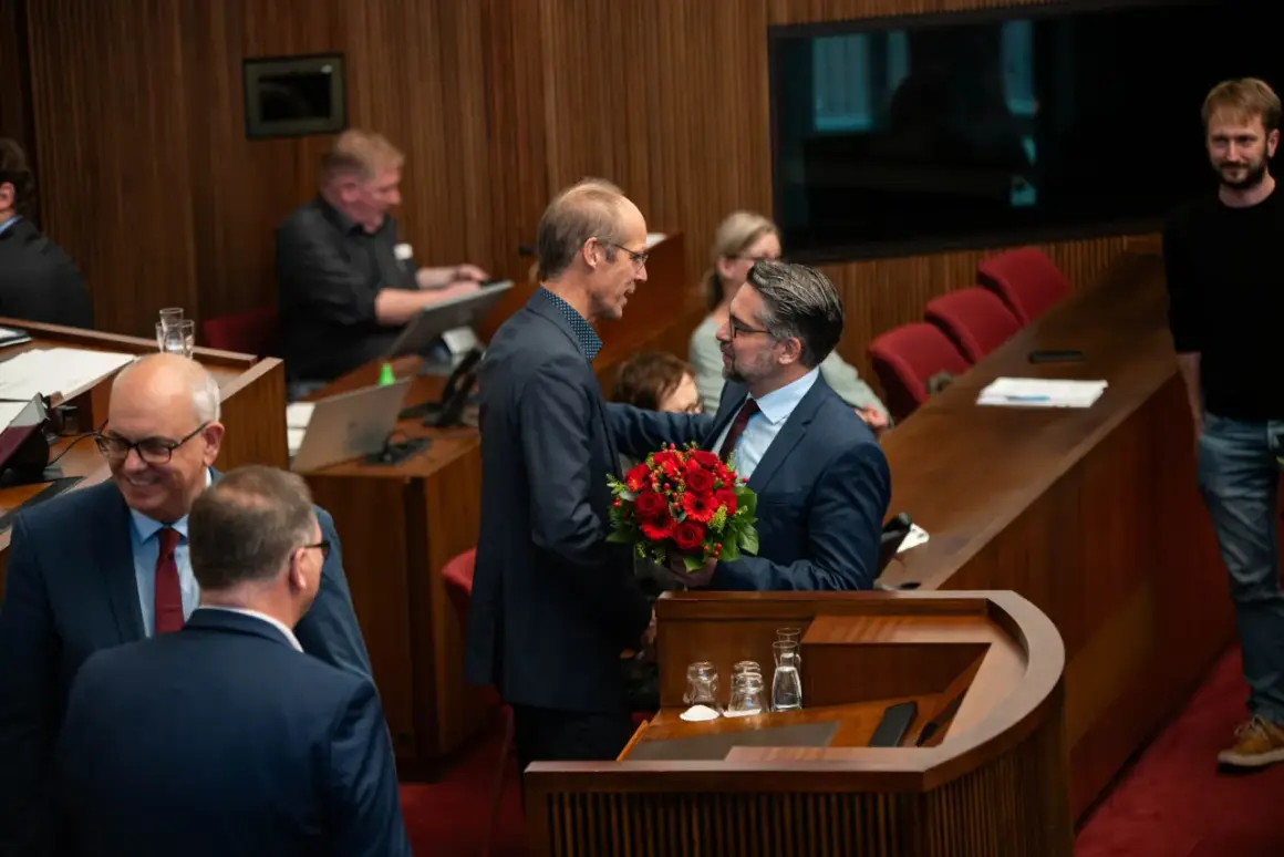 Ein Mann überreicht Mark Rackles einen Blumenstrauß in einem Sitzungssaal.