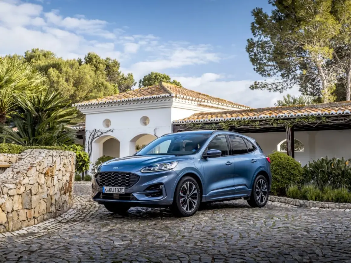 Niebieski Ford SUV Kuga, jeden z popularnych ford suv modele, zaparkowany na brukowanym podjeździe przed białym domem z czerwoną dachówką.