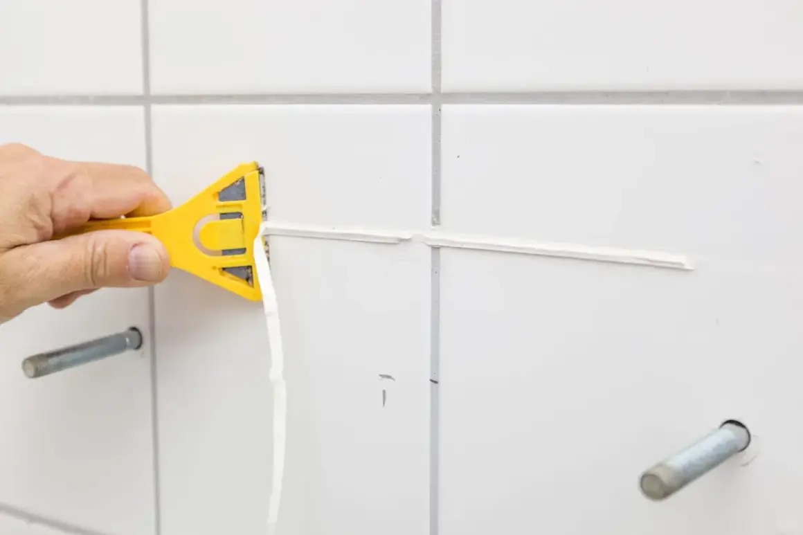 Main jaune en action pour enlever silicone vinaigre. Le joint est retiré proprement.