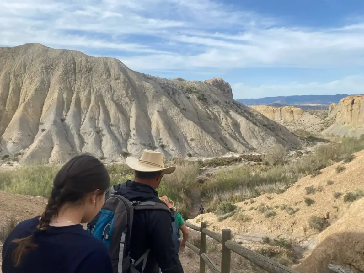 Senderos para visitar el desierto de Tabernas gratis. Familias exploran paisajes áridos bajo un cielo azul con nubes.