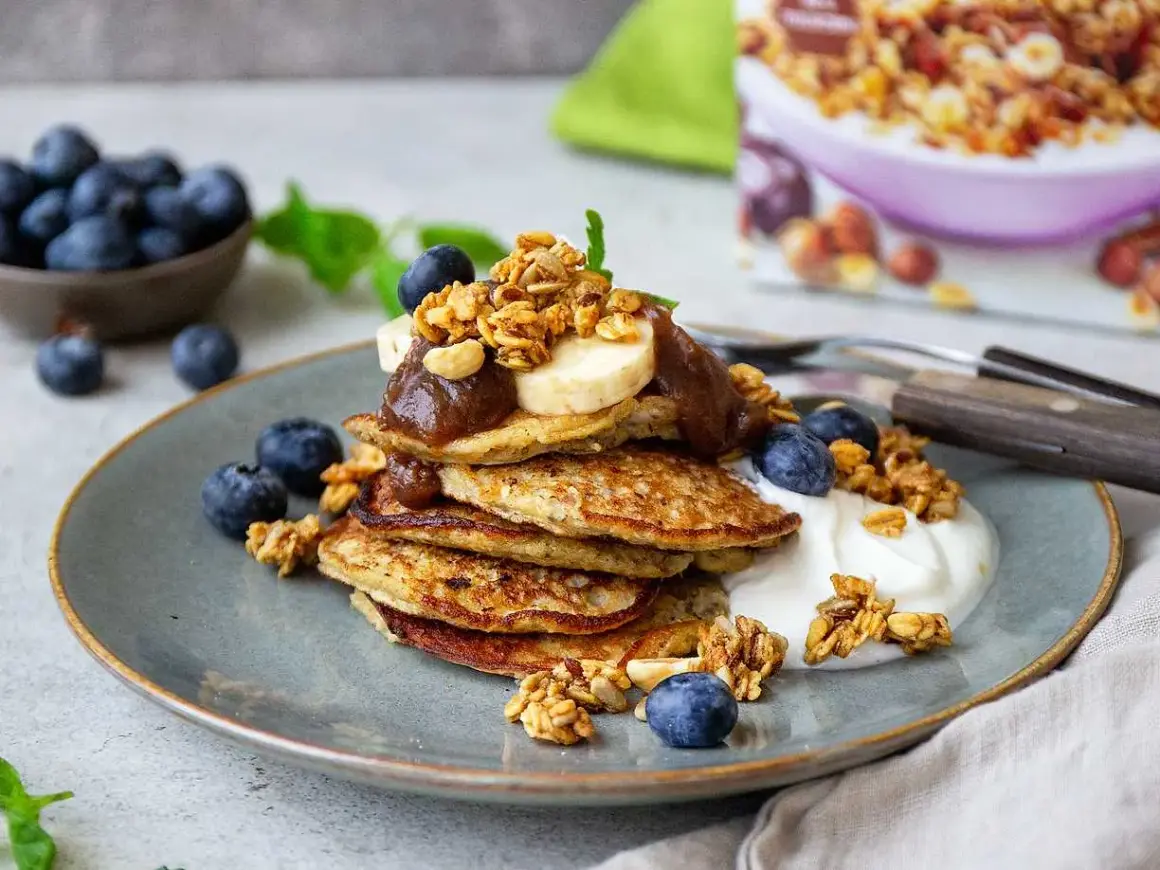 En hög med bananpannkakor toppas med banan, sylt och granola. Ett perfekt bananpannkaka recept för en lyxig frukost eller brunch.