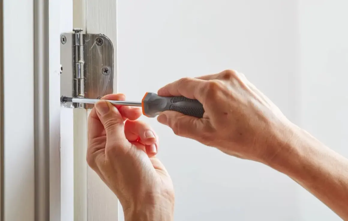 Mains serrant une vis avec un tournevis pour réparer une porte qui grince.