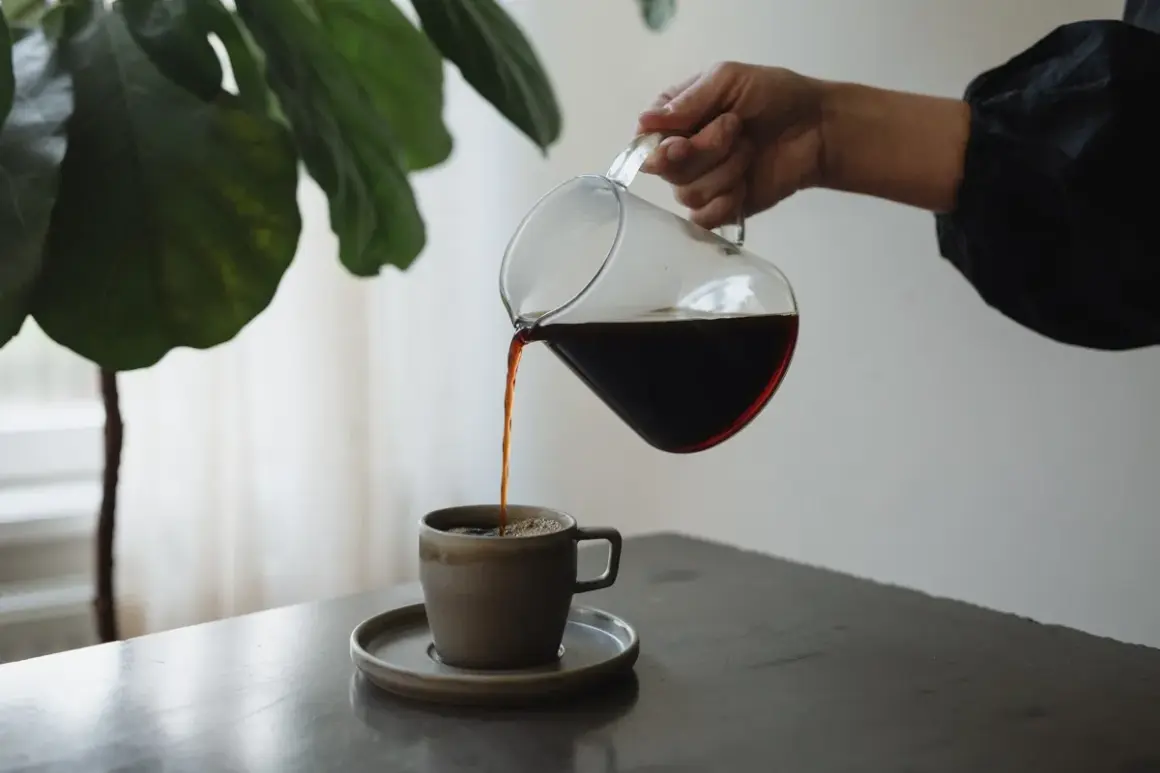 En hand häller upp mörkt kaffe ur en glaskanna i en mugg. Kaffet innehåller njutning och energi.