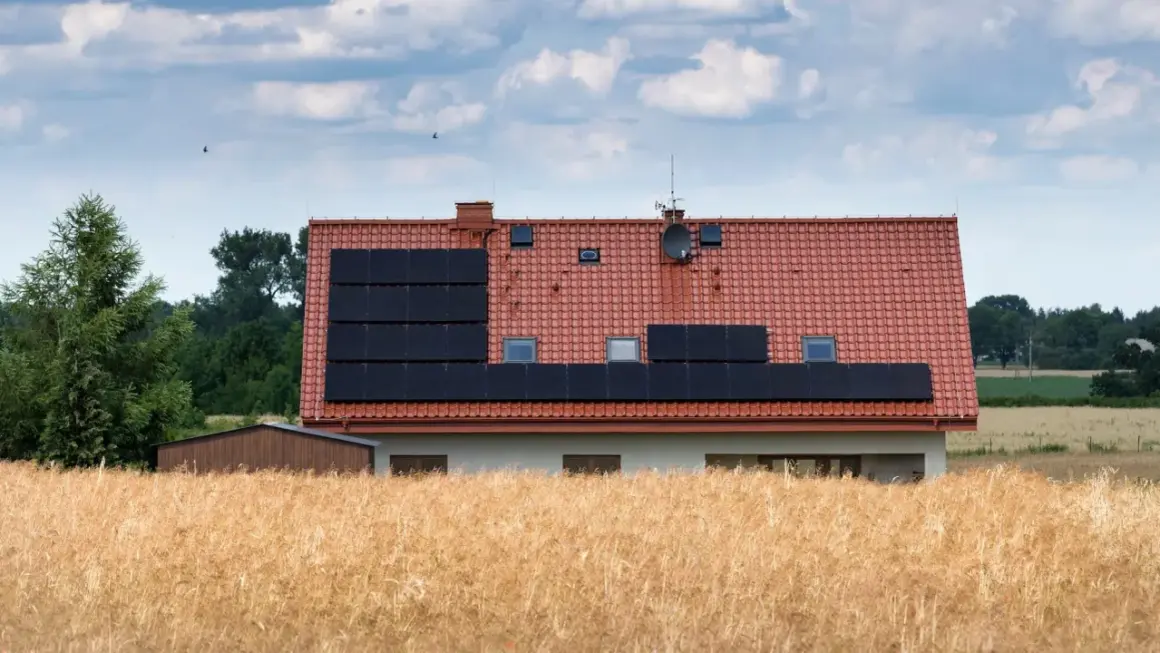 Dom z panelami słonecznymi na dachu, otoczony polami. Może to być znak, że nawet w spokojnej okolicy zdarzają się problemy z za wysokie napięcie w sieci.