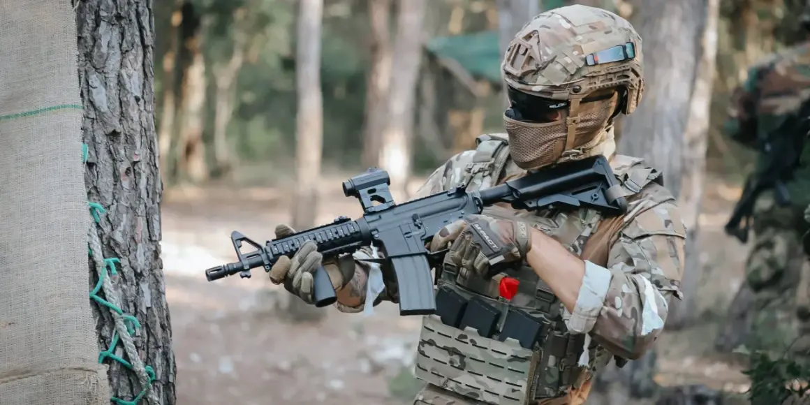 Jugador de fps airsoft con casco y rifle táctico, listo para la acción en un bosque.