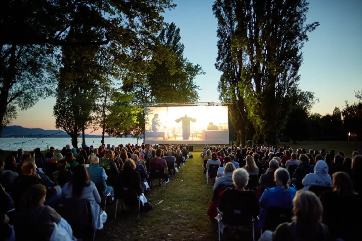 Open-air Kino in Boxberg: Viele Menschen sitzen auf Stühlen und schauen einen Film auf einer großen Leinwand am Seeufer.