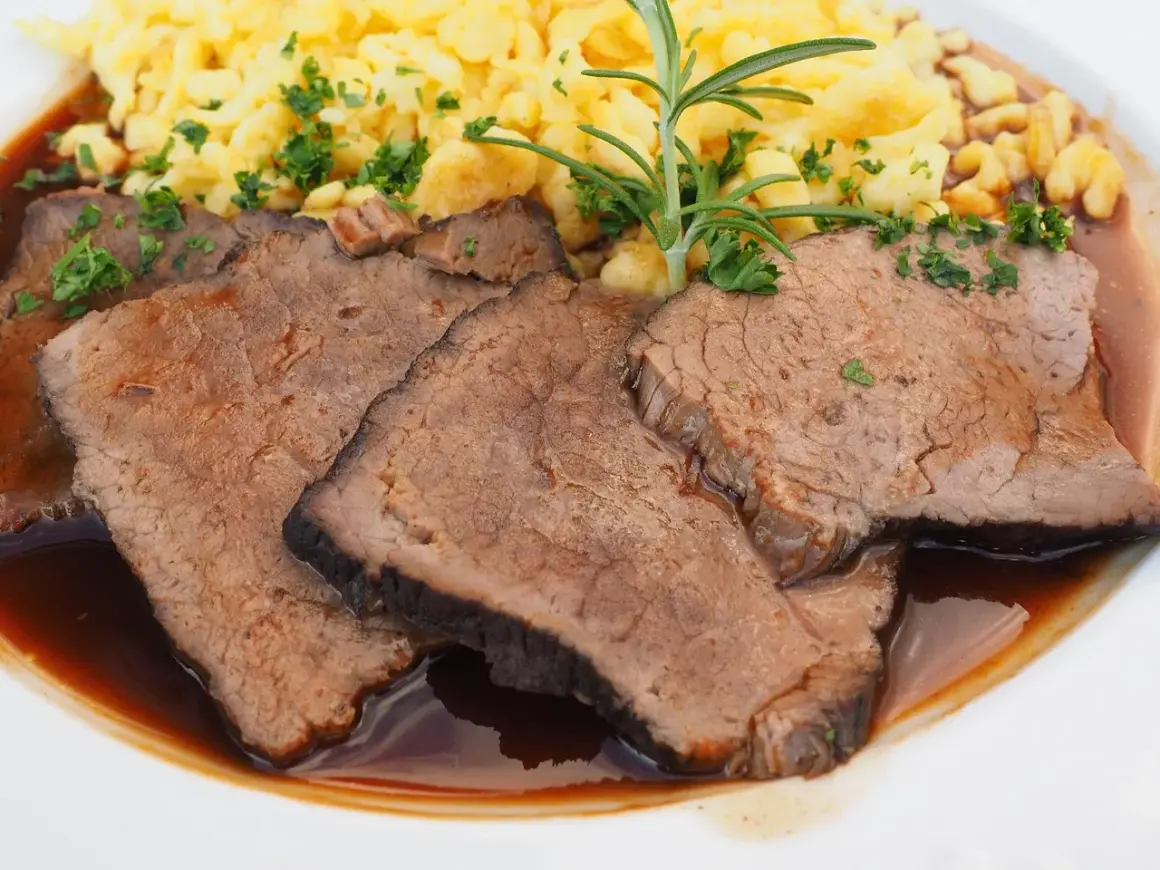 Fertig eingelegter Sauerbraten zubereiten: Zarte Scheiben Rindfleisch in dunkler Sauce mit Spätzle und Rosmarin garniert.