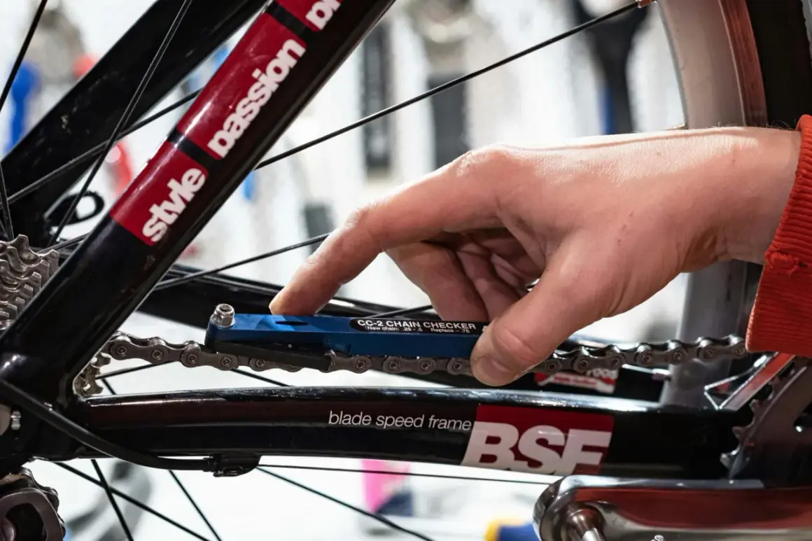 Hand gebruikt een blauwe kettingmeter om te controleren of het tandwiel van de fiets vervangen moet worden.