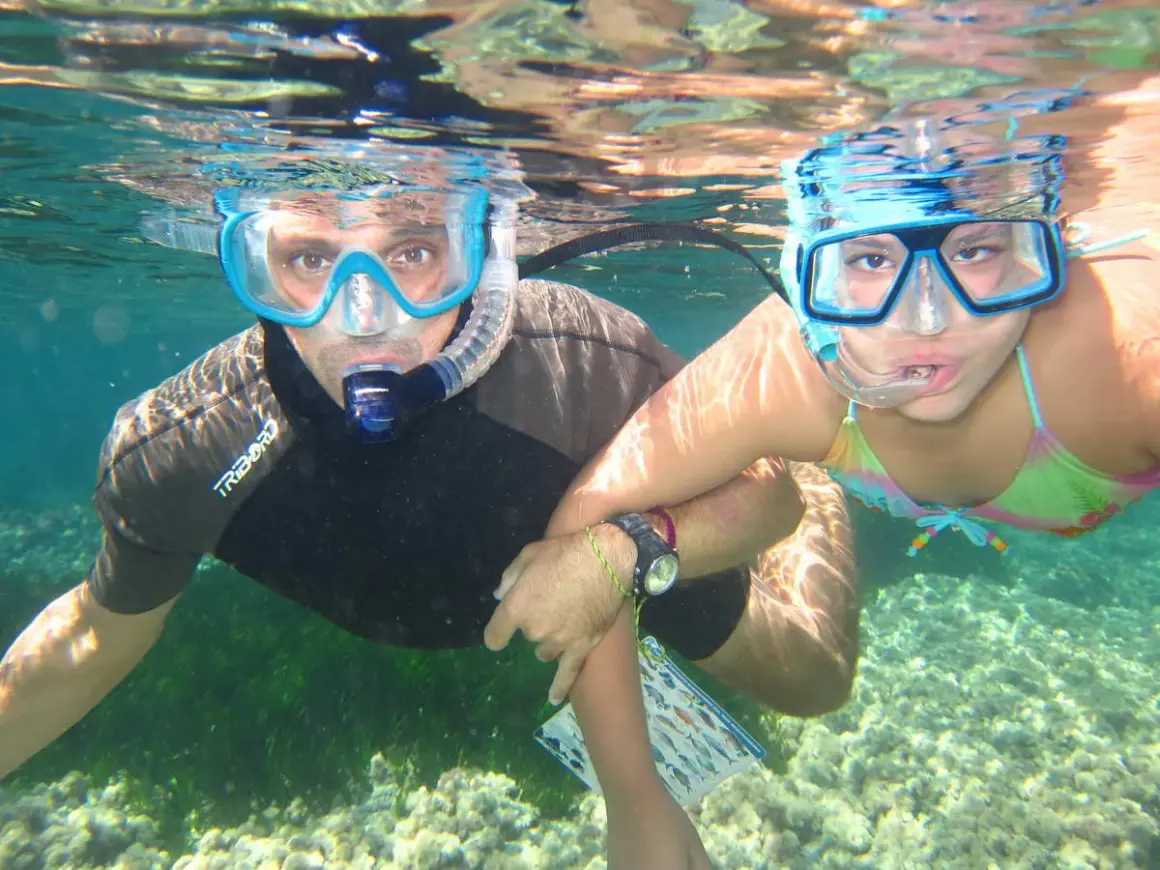 Padre e hija disfrutan del snorkel en la playa de los Muertos, explorando el fondo marino.