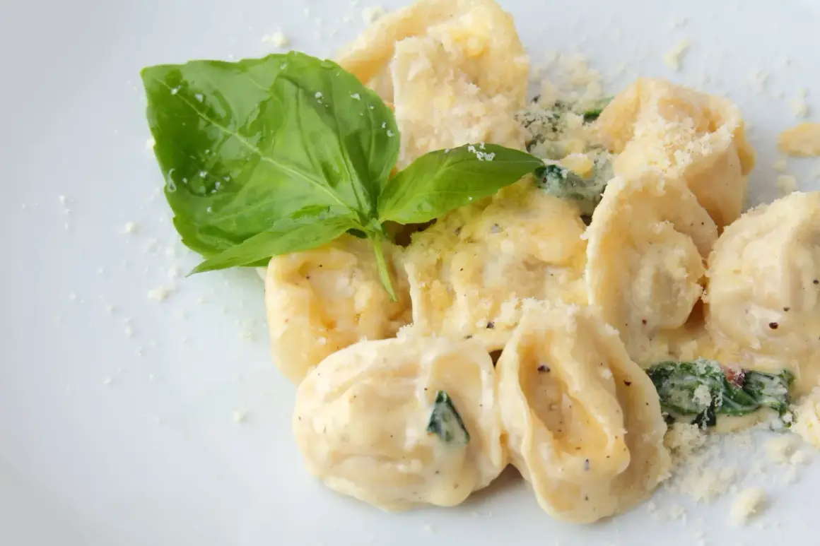 Pyszne ravioli w kremowym sosie, posypane parmezanem i udekorowane listkiem bazylii. Idealne danie, które podpowiada, ravioli z czym podawać.
