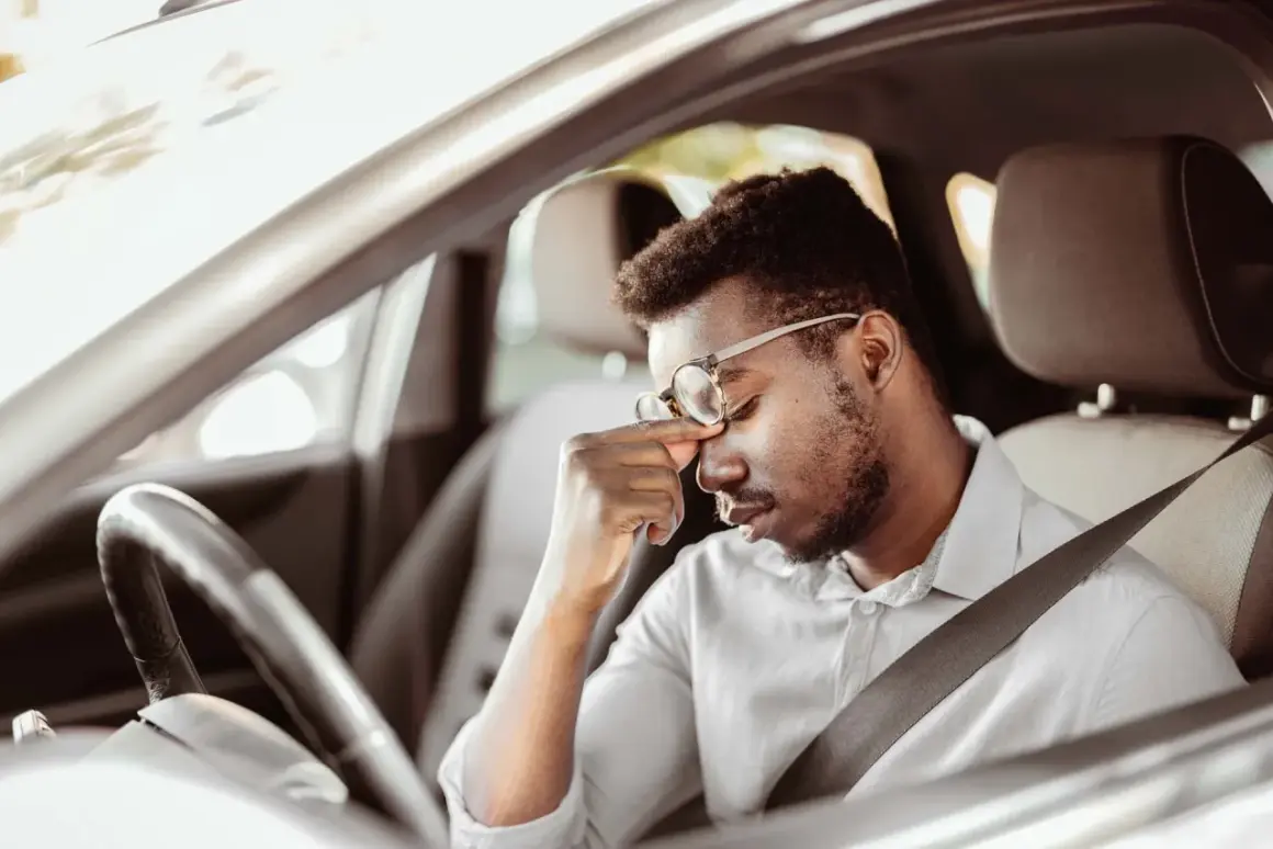Erschöpfter Mann mit Brille reibt sich die Augen, während er im Auto sitzt. Die lange Fahrt ermüdet ihn.
