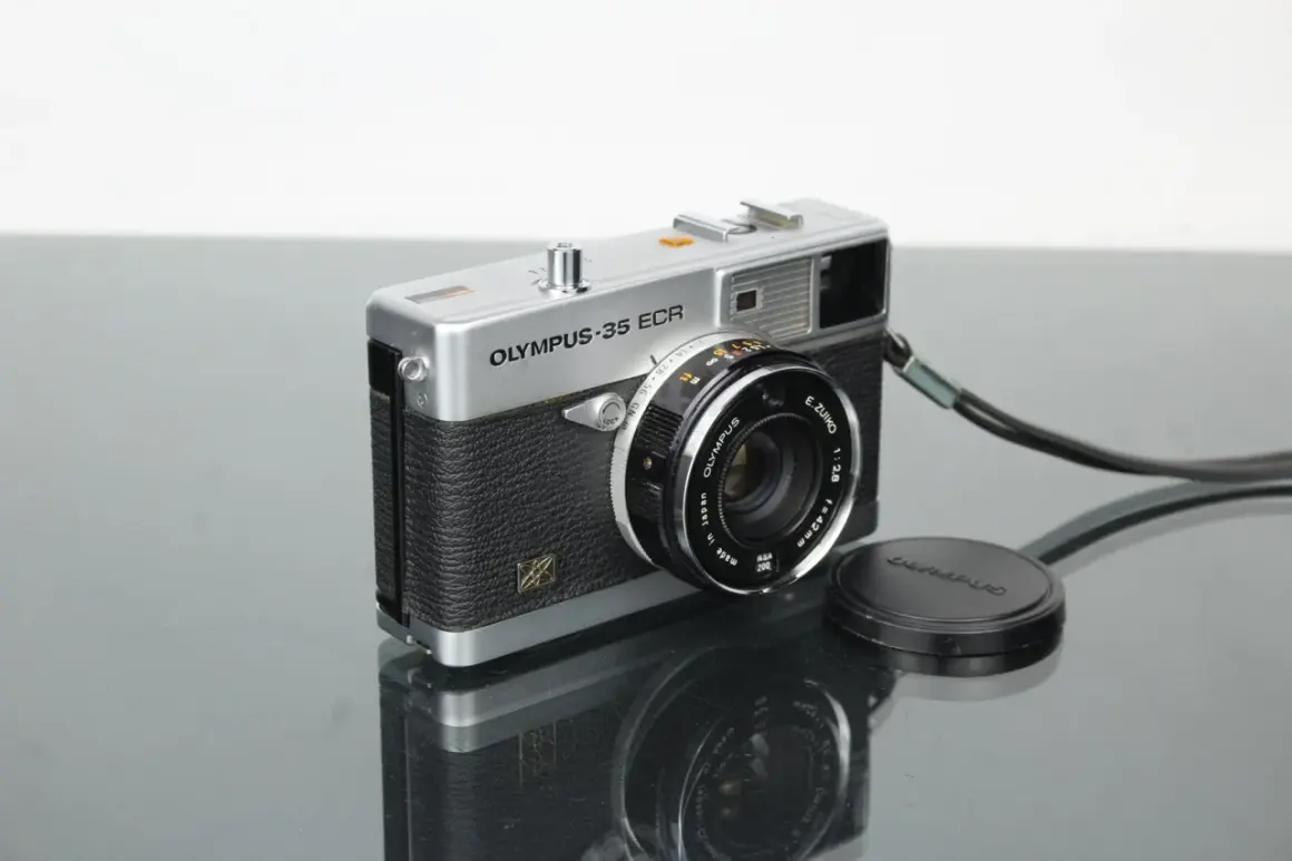 A vintage silver Olympus 35 ECR rangefinder camera with a black textured grip sits on a reflective surface.