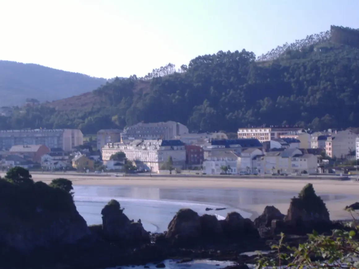 Vista de la playa vivero con edificios y colinas verdes al fondo.