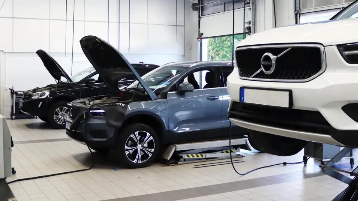 Flera Volvo-bilar, inklusive en vit XC40 och en grå elbil, på verkstad för volvo classic service. Motorhuvar öppna för inspektion.