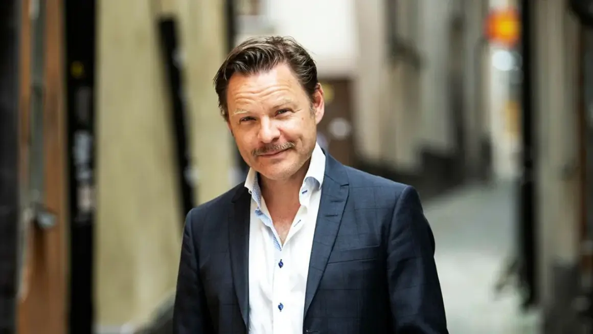 Kasper Sulocki, en man med mustasch, bär en mörkblå rutig kavaj och vit skjorta i en gränd.