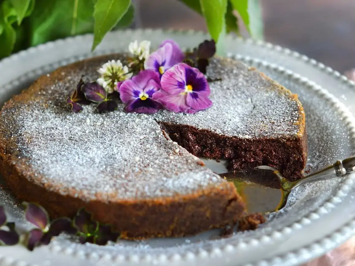 En saftig tårta med chokladpudding, pudrad med florsocker och dekorerad med violer och klöver. En bit är uppskuren.