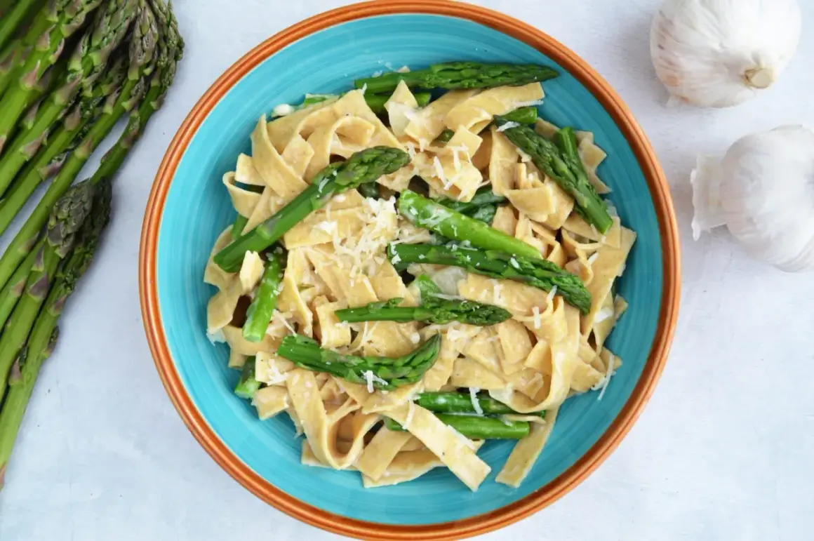 Makaron tagliatelle z zielonymi szparagami i startym parmezanem w niebieskiej misce.