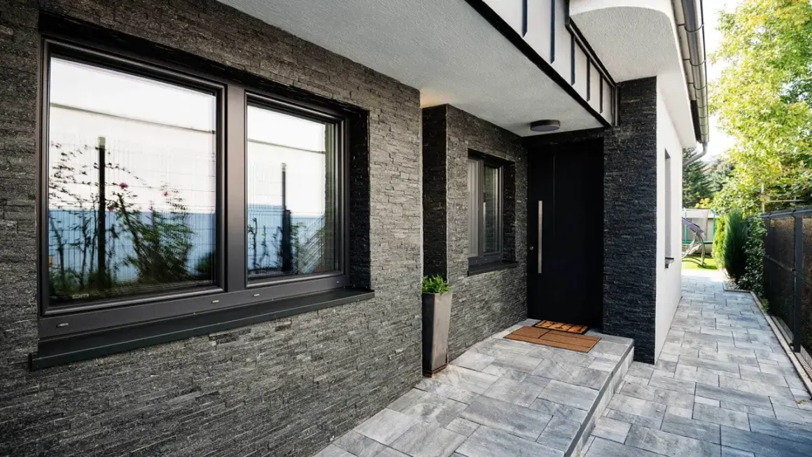 Nowoczesny dom z kamienną elewacją i czarnymi oknami. Świetny pomysł na elewację domu, który nadaje mu elegancki i minimalistyczny charakter.