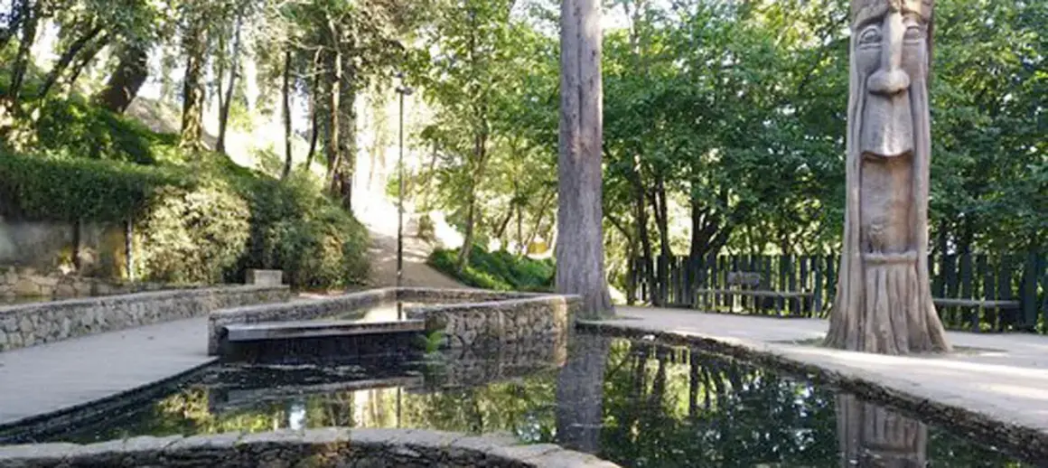Escultura de madera en el parque de los sentidos, junto a estanques de agua y vegetación exuberante.