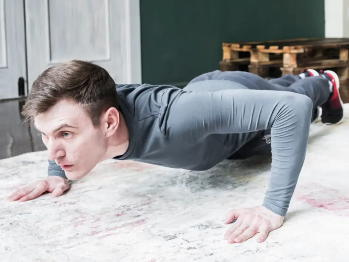 Un homme en tenue de sport fait des pompes tous les jours sur un tapis. Il est concentré et déterminé.