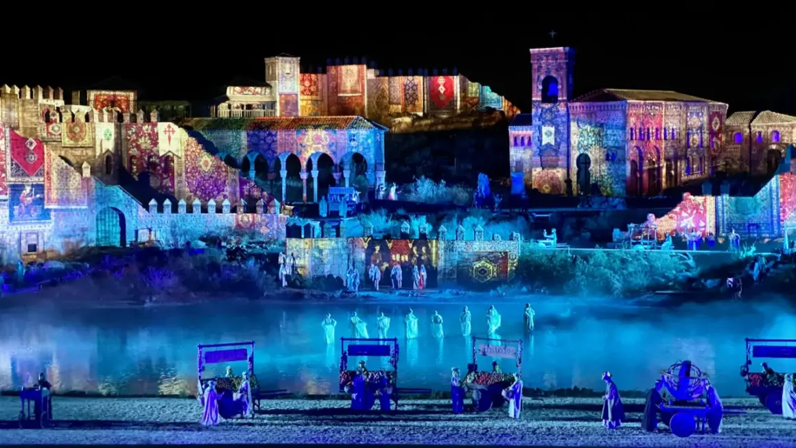 Espectáculo nocturno en Puy du Fou, Francia. Edificios históricos iluminados con proyecciones de tapices y figuras danzando en el agua.