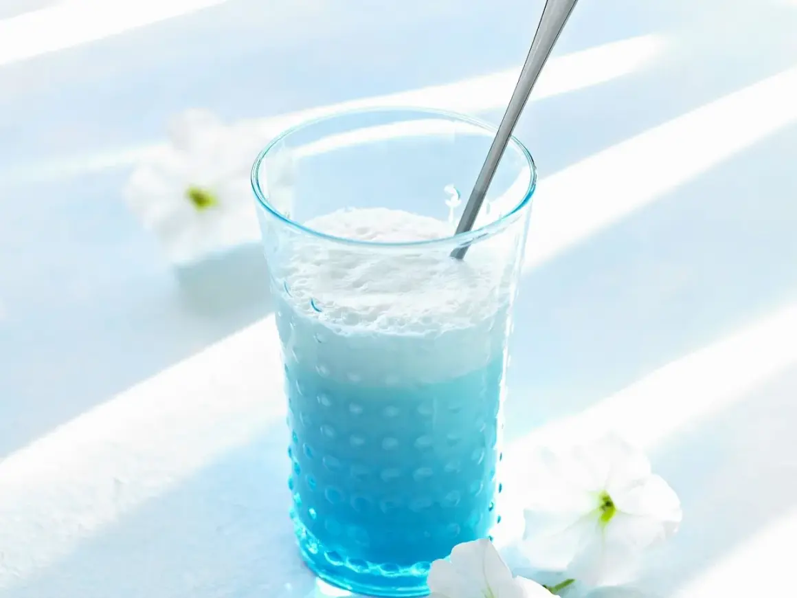 Ein erfrischender Blue Curacao Cocktail in einem strukturierten Glas, garniert mit weißen Blüten.