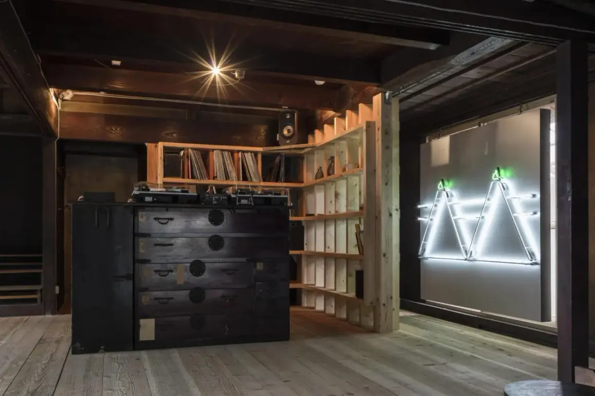 Theaster Gates studio: A DJ setup sits atop a dark wooden chest of drawers, surrounded by shelves of records and a striking neon art installation.