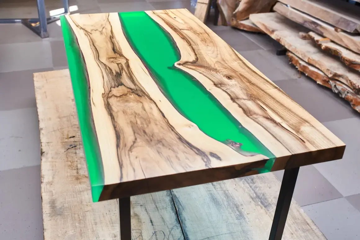 Tavolo con resina verde brillante tra venature di legno. La differenza tra levigatura e lucidatura è evidente nella finitura liscia e riflettente.