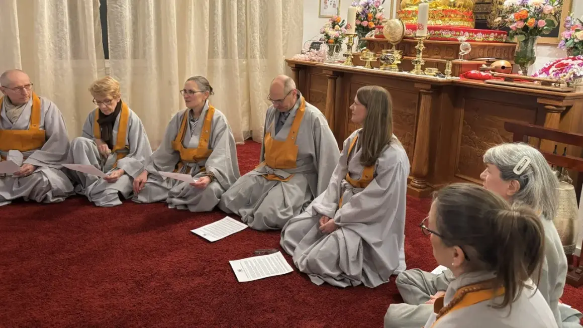 Menschen in buddhistischen Roben sitzen auf einem roten Teppich und lesen buddhistische Mantratexte.