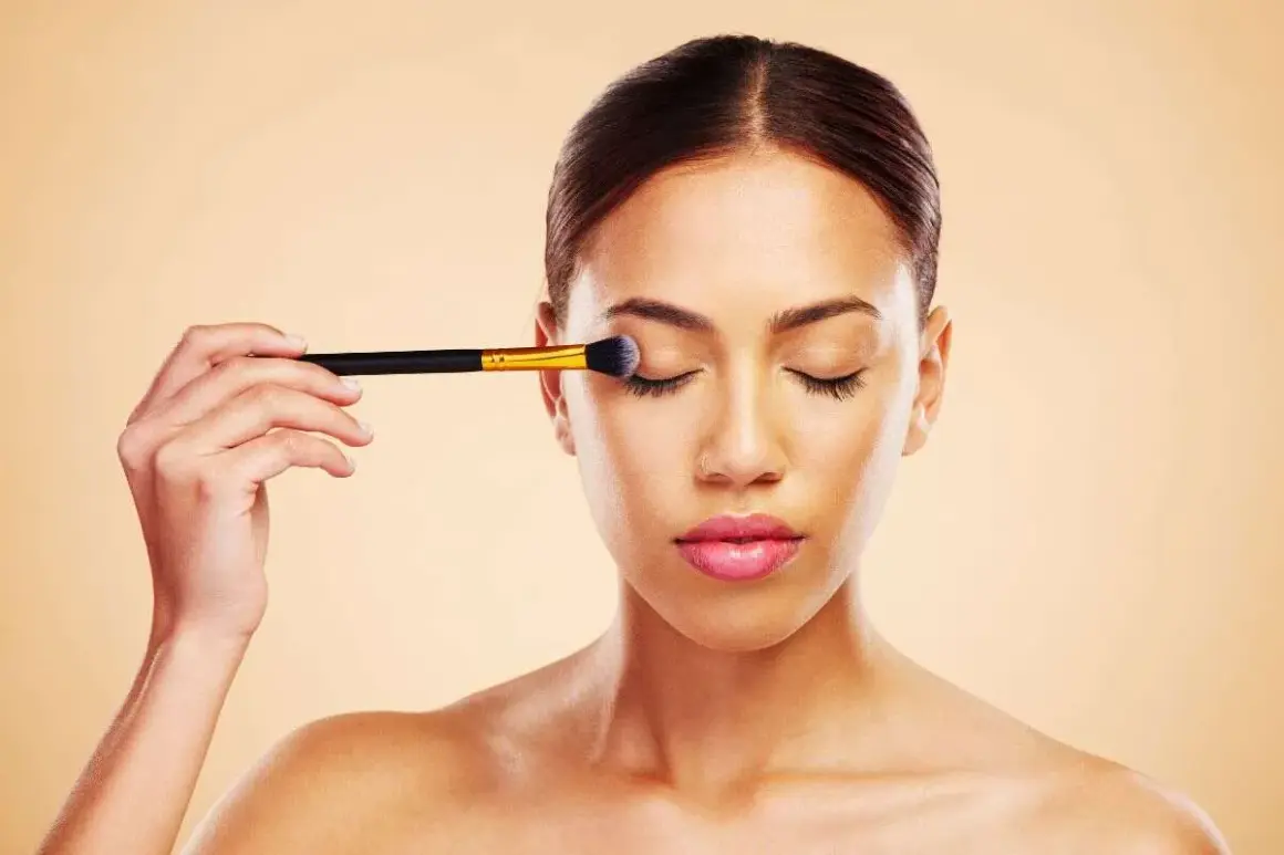 Donna applica ombretto con un pennello, un passo fondamentale per un make up perfetto.