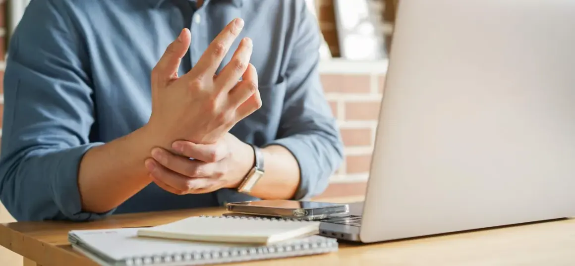 Uomo con male ai polsi mentre lavora al computer. Dolore al polso da uso prolungato del mouse e tastiera.