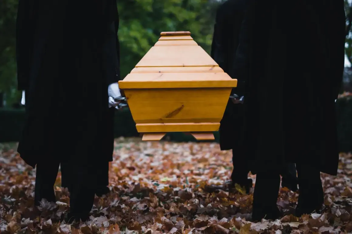 Pogrzebowi noszą drewnianą trumnę pośród jesiennych liści. Kto nie dostanie zasiłku pogrzebowego, ten sam musi zadbać o godny pochówek.