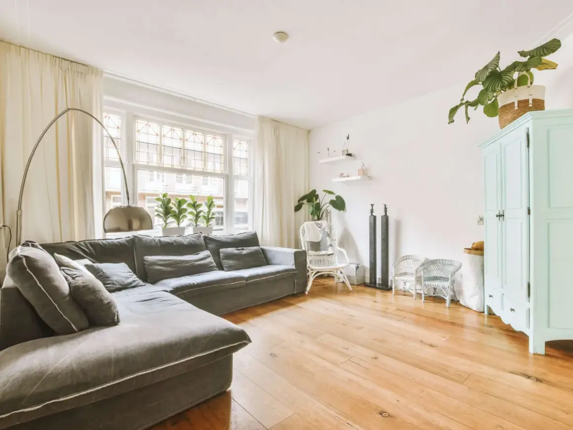 Gemütliches kleines Wohnzimmer einrichten mit großem Ecksofa, Bogenlampe, Pflanzen und mintgrünem Schrank.