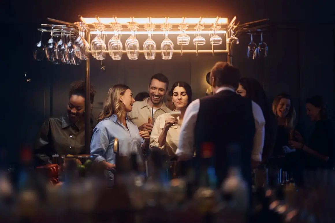Glada gäster minglar och skrattar vid baren på Gothia Towers Skybar. Glas hänger i taket, redo för drinkar.