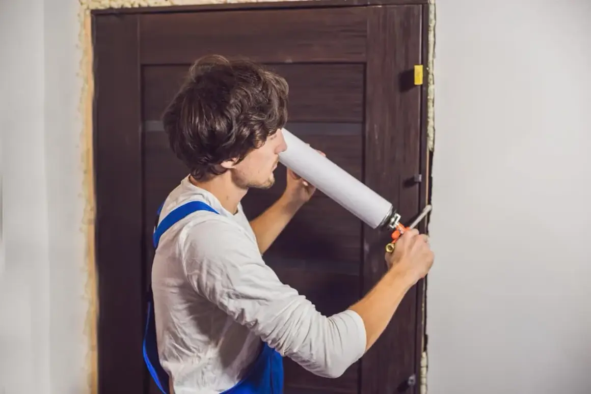 Un homme utilise une mousse expansive pour comment isoler une porte. Il applique le produit dans l'encadrement.