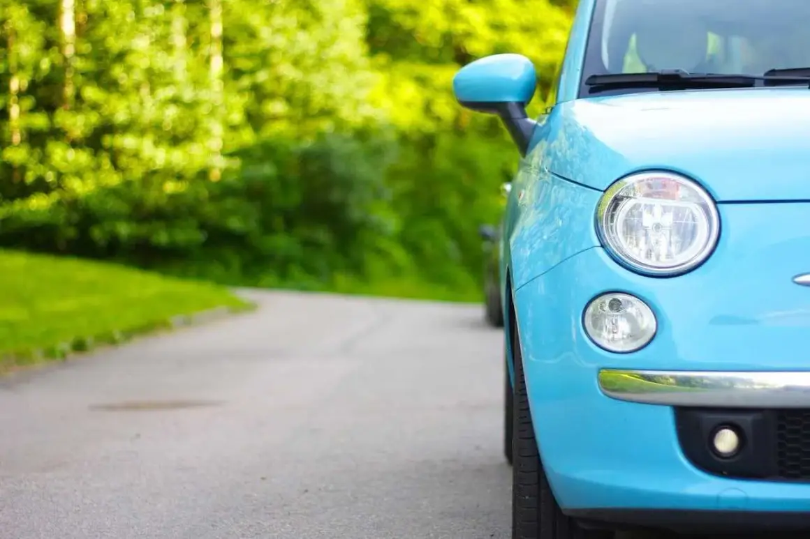 Niemiecki cepik, błękitny Fiat 500, parkuje na krętej drodze wśród zieleni.