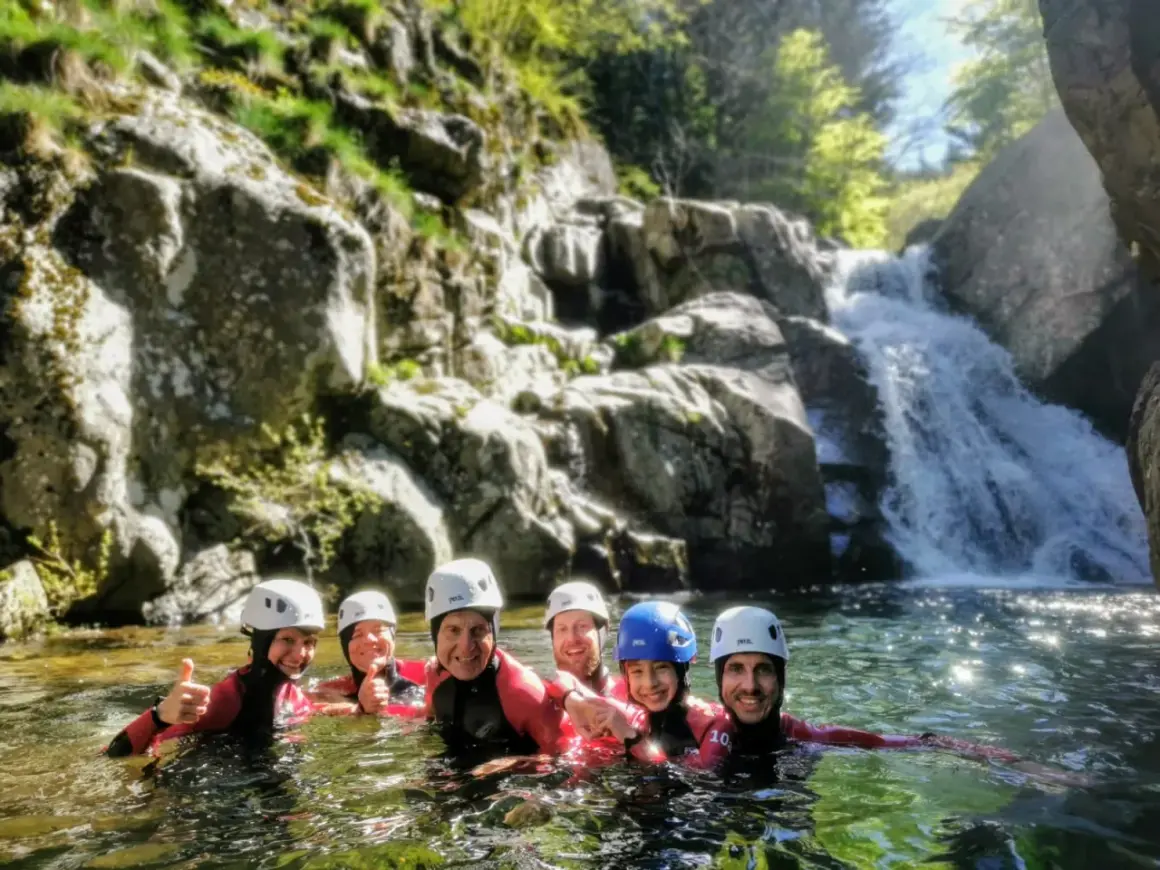 Groupe souriant en combinaison néoprène, casques blancs et bleus, profitant d'une descente en canyoning près d'une cascade. Une belle aventure de canyoning dans le Vallon Pont d'Arc.