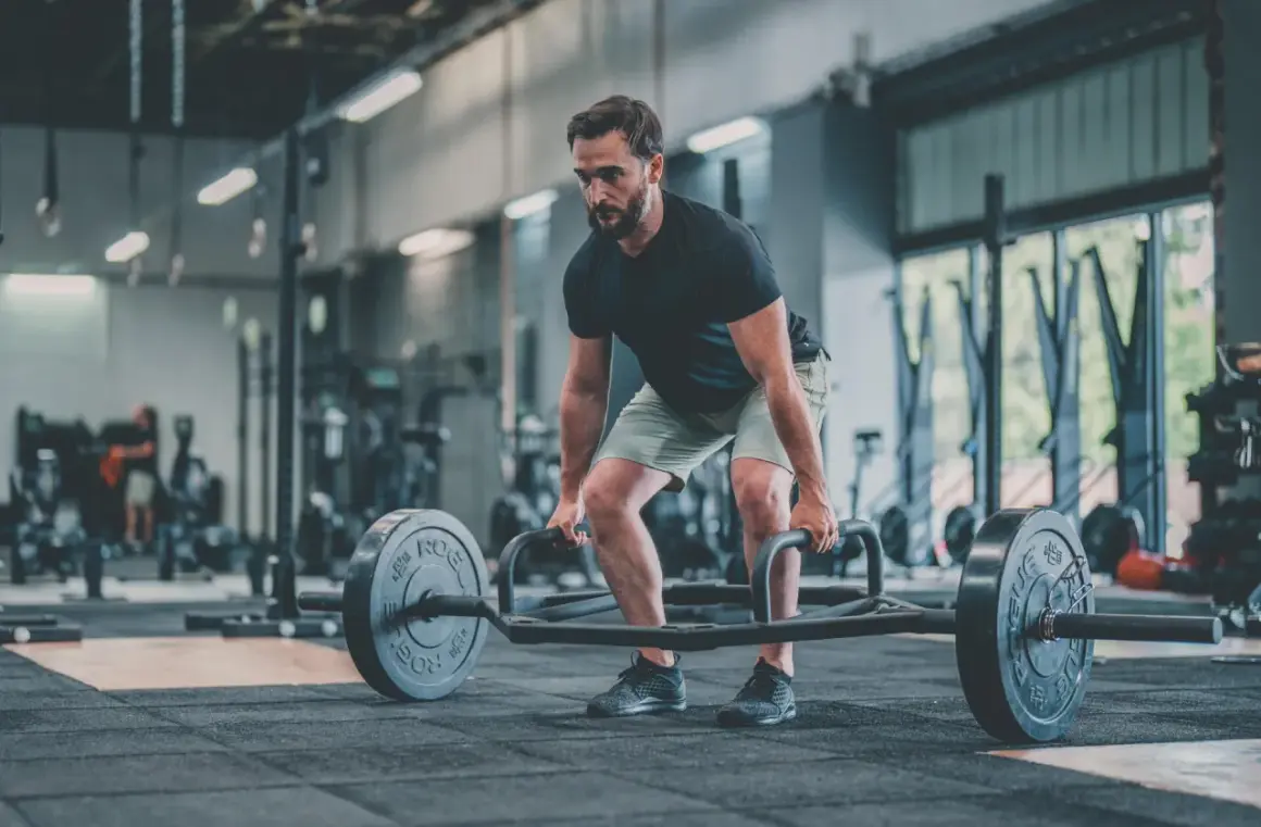 Un homme concentré effectue un dead lift avec une barre hexagonale dans une salle de sport.