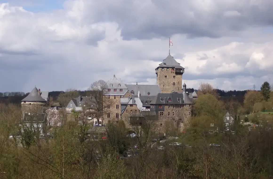 Das Schloss Burg an der Wupper, eine imposante Burganlage mit Bergfried und vielen Gebäuden, thront über Bäumen.