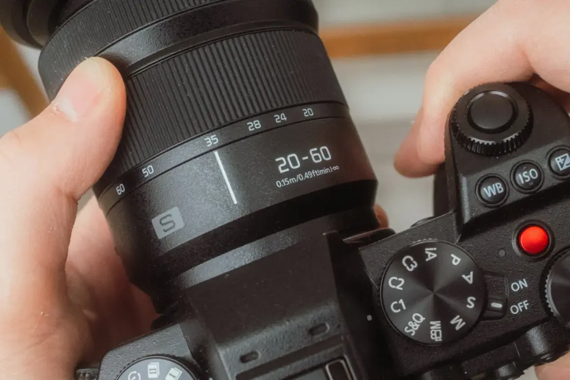 Dłonie trzymają aparat, obracając pierścień z oznaczeniami 20-60 mm. To właśnie zoom, czyli możliwość zmiany ogniskowej obiektywu.