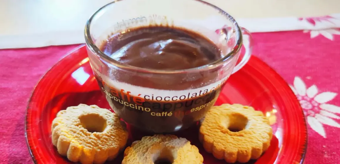 Bicchiere di cioccolata calda con acqua senza fecola, accompagnata da biscotti su un piatto rosso.