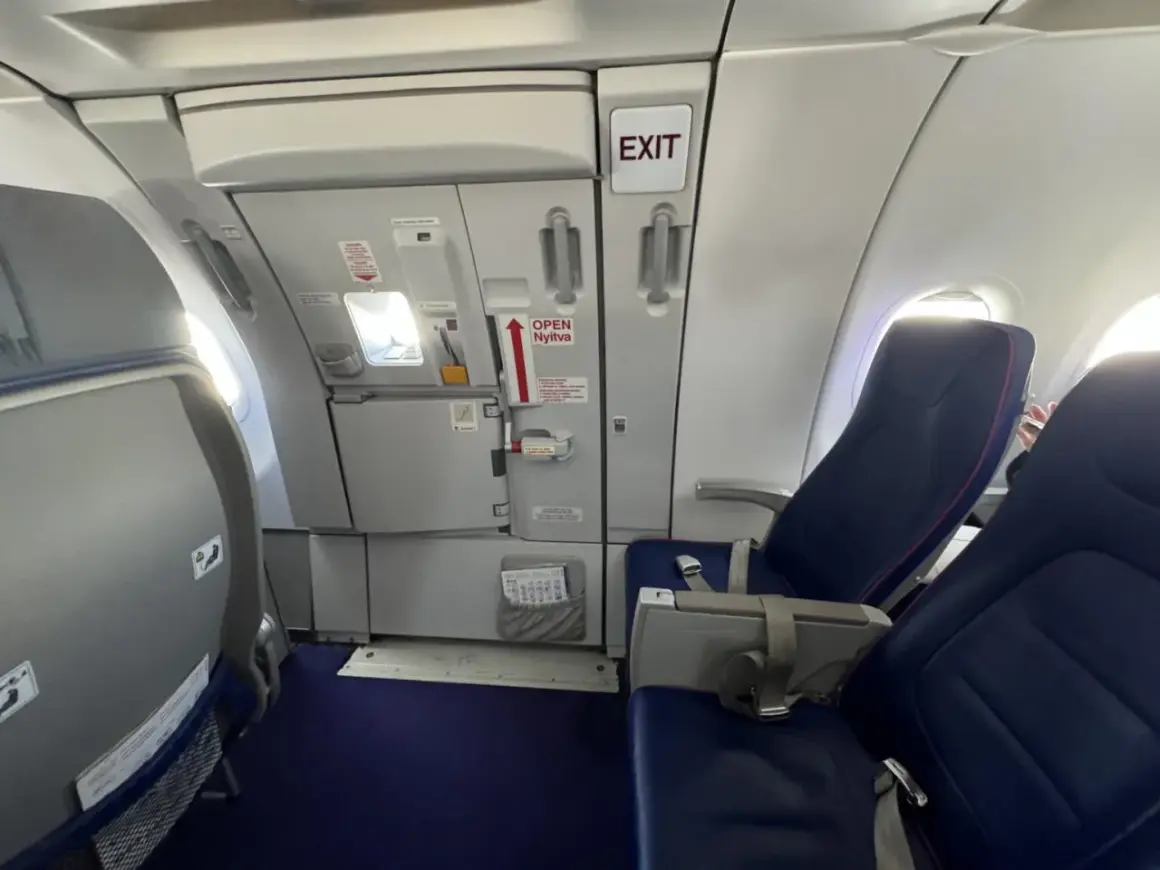 Wnętrze samolotu Wizzair. Widok na rząd siedzeń i drzwi wyjściowe. Numeracja miejsc w samolocie Wizzair jest widoczna na siedzeniach.