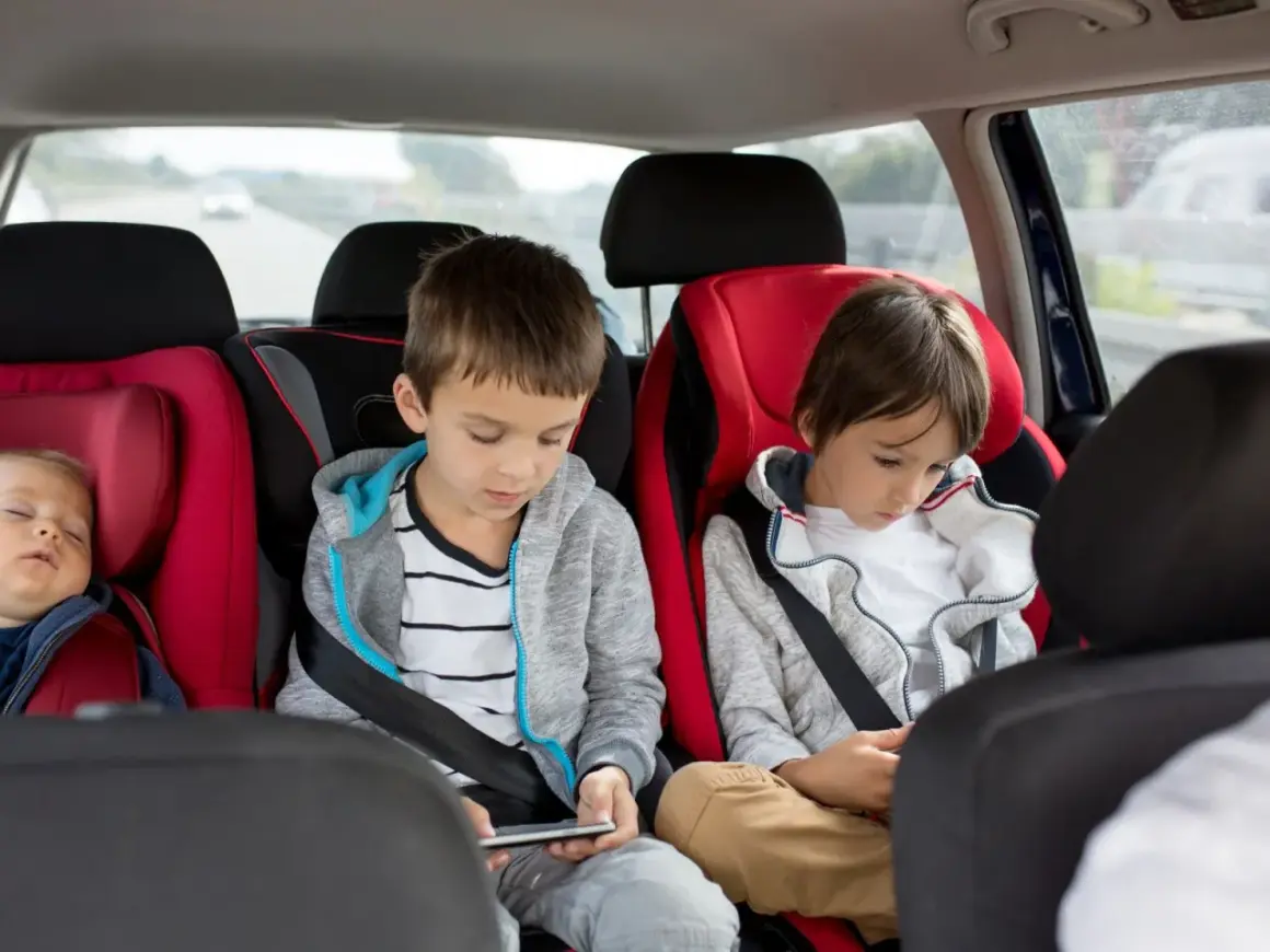 Im Auto mit 3 Kindern: Ein Baby schläft, die älteren Brüder sind mit ihren Handys beschäftigt.