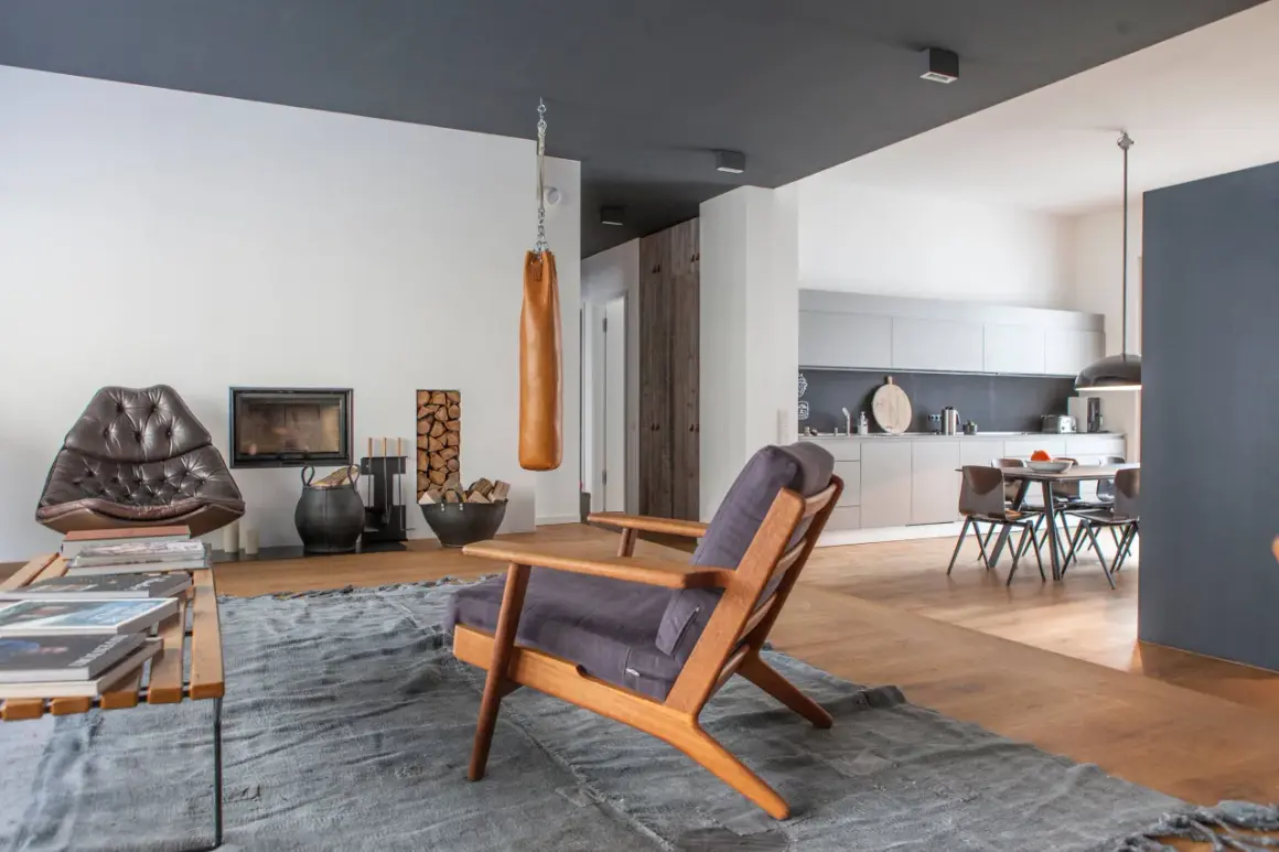 Ein Wohnzimmer mit Kamin, Ledersessel und einem Holzstuhl. Die Kombination von Holzarten im Boden und Möbeln schafft eine warme Atmosphäre.