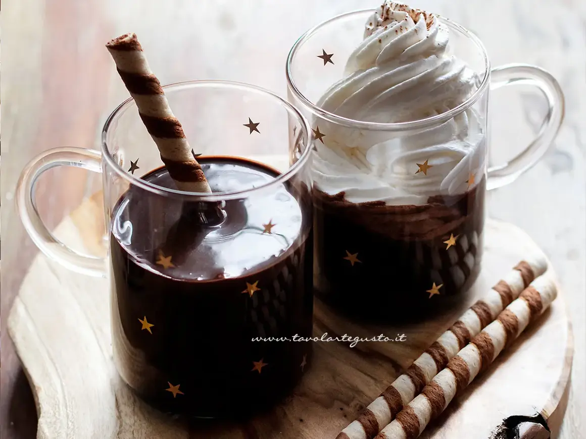 Due tazze di cioccolata calda con cacao e latte, una con panna e cacao, l'altra con un biscotto.